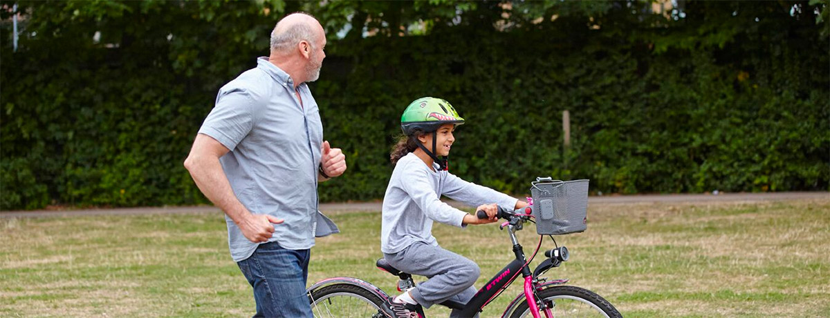 Dad jogging alongside a young girl learning to ride her bicycle 