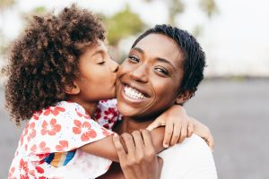 youthful , happy black African, Caribbean , woman receiving a kiss on the cheek from her black daughter